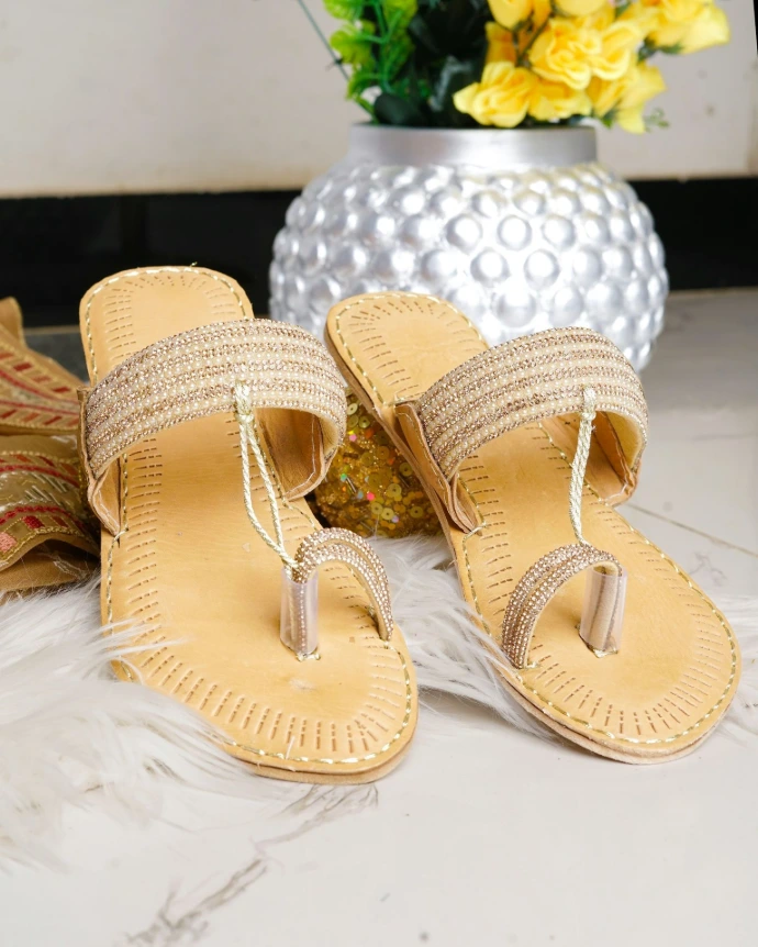 A pair of embellished flat sandals on a marble surface.